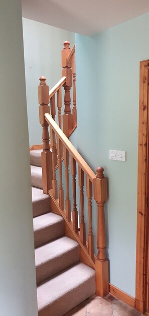 Una escalera con balaustres de madera y un rellano cubierto de alfombra beige.