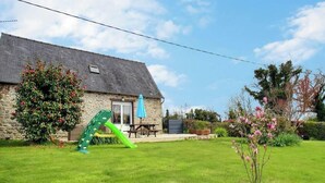 Una casa in pietra con un patio, uno scivolo verde e un giardino con piante fiorite.