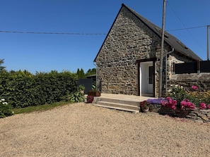 A stone building with a sloped roof, a gravel driveway, and a variety of flowers in front. - Goas Raoul - PLEUMEUR GAUTIER (PLEUMEUR GAUTIER)