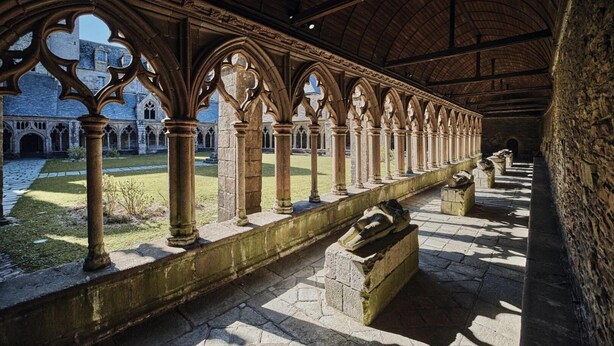 Un chiostro con colonne e archi in pietra, un cortile e una vista su un edificio con facciata in pietra.