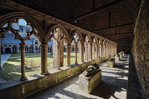 A cloister with stone columns and arches, a courtyard, and a view of a building with a stone facade. - Goas Raoul - PLEUMEUR GAUTIER (PLEUMEUR GAUTIER)