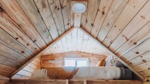 A wooden cabin with a sloped ceiling, a bed, and a small window. - Cozy tiny home with Sunrise Views in the Heart of Finger Lakes (Penn Yan)