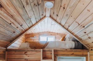Una cabaña de madera con techo inclinado, una cama y un ventanal pequeño.