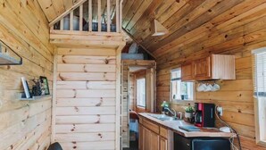 A cabin interior with a sofa, kitchen area, and a staircase leading to a loft. - Cozy tiny home with Sunrise Views in the Heart of Finger Lakes (Penn Yan)