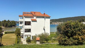 A white building with a red-tiled roof, a balcony, and a view of the sea.