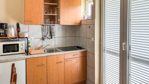 A kitchen with wooden cabinets, a microwave, a sink, and a window with blinds.