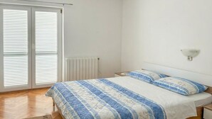 A bedroom with a bed, a radiator, a nightstand, a wall-mounted lamp, and a sliding glass door.