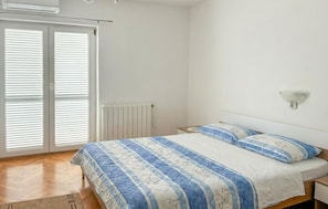 Une chambre à coucher comprenant un lit, un radiateur, une table de chevet, une lampe fixée au mur et une porte-fenêtre coulissante.