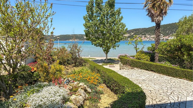 A landscaped garden with a stone pathway, various plants, and a view of the sea.