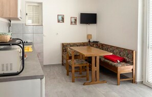 Una cocina compacta con zona de comedor, un televisor montado en la pared y una ventana con persianas.