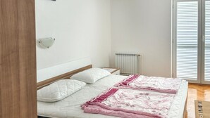 A bedroom with a bed, a bedside table, a radiator, and a window with blinds. - 1 bedroom cozy apartment in Rab Sup.Draga (Rab Sup.Draga)