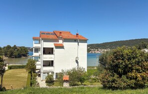 A white building with a red-tiled roof, a balcony, and a view of the sea.