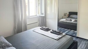 Une chambre à coucher avec un lit, une table de chevet, un miroir et une fenêtre avec des rideaux.
