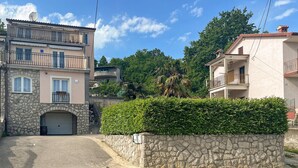 Une rue résidentielle bordée de murs en pierre, avec un garage et une haie bien entretenue.