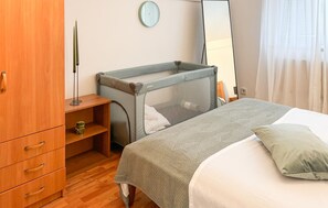 Ein Schlafzimmer mit einem Bett, einem Babybett, einem Holzschrank, einer Uhr und einem Fenster mit Vorhängen.