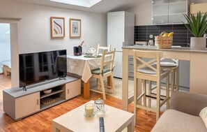 Ein modernes Wohnzimmer mit Flachbildfernseher, einem Essbereich mit Tisch und Stühlen, einer Küche mit schwarzem Fliesenspiegel und Kunstwerken an der Wand.