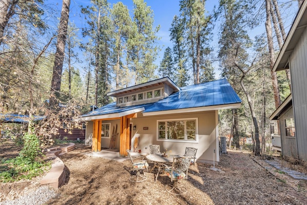 Une maison avec un toit bleu, un patio couvert avec des chaises et une vue sur de grands arbres.