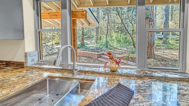 Una cocina con encimeras de granito, un fregadero de acero inoxidable y una ventana con vistas a zona boscosa.