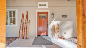 Entrada a una cabaña de esquí con una puerta de madera, esquíes apoyados en la pared y un portaesquíes.