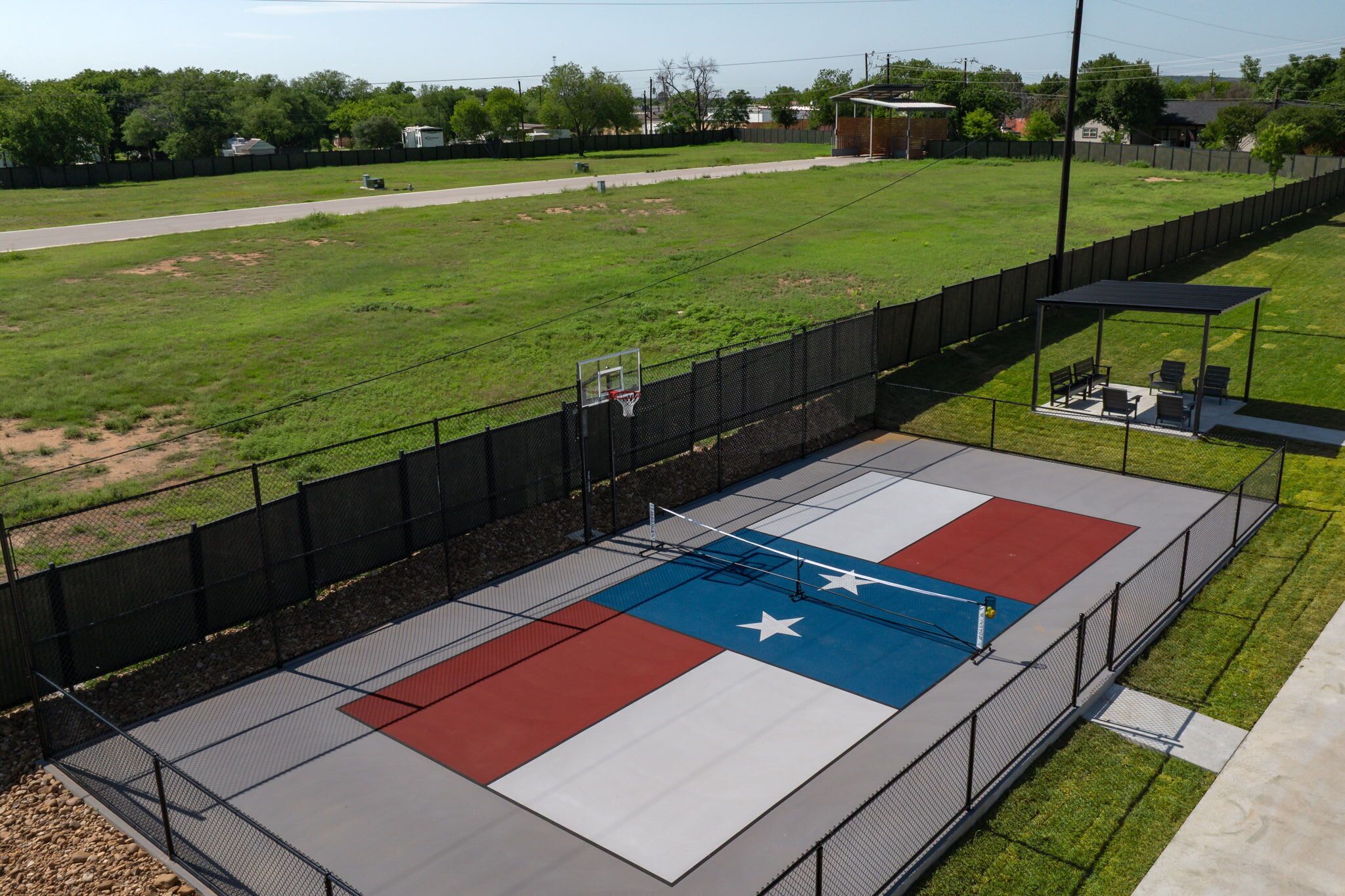 Een basketbalveld buiten met een ontwerp van de Texas vlag, omringd door een hek, en een overdekt zitgedeelte.