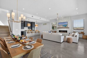 A modern living room with a dining area, white sofas, a fireplace, and a large window with a view.