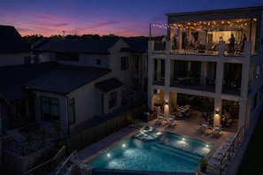 A multi-story building with a swimming pool, outdoor seating, and string lights.