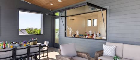 Un área de comedor exterior moderna con una mesa, sillas y una barra provista de botellas.