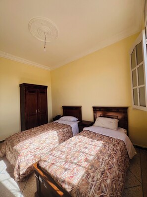 Une chambre avec deux lits, une armoire en bois, une fenêtre et un luminaire au plafond.