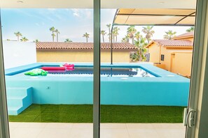 A swimming pool with a blue interior, surrounded by artificial grass, and palm trees in the background. - Casa Descanso (Puerto Peñasco)
