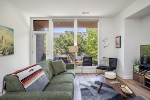 Ein modernes Wohnzimmer mit Sofa, Couchtisch, Fernseher und Blick durch große Fenster.