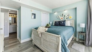 Une chambre à coucher comprenant un lit, une table de chevet, une commode, un mur décoré sur le thème de la marine, et une porte donnant accès à une salle de bain.