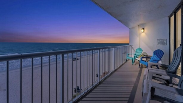 Un balcon avec vue sur l’océan au coucher du soleil, une balustrade et deux chaises.