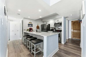 Eine moderne Küche mit Kochinsel, Barhocker, Kühlschrank, Mikrowelle, Backofen und einer Holztür.