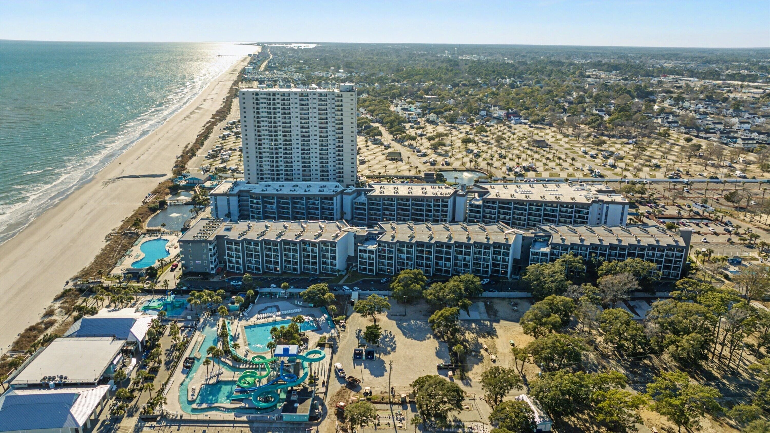 A coastal hotel with a large building, a pool area, and a beach view.