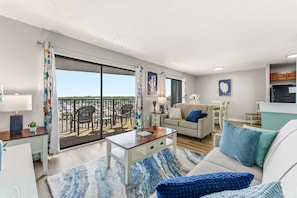 A modern living room with a sofa, coffee table, and a dining area with chairs. - MB Ocean Spa 526-Ocean view, Great Amenities (Myrtle Beach)