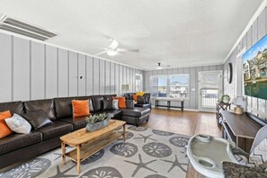 Ein Wohnzimmer mit einem Ecksofa, einem Holztisch und Blick auf ein Gewässer durch große Fenster.