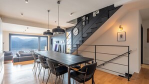 A modern kitchen with a large island, a staircase with a black railing, and a view of the mountains. - Lake Como View 3BR | Regina 35 (Carate Urio)