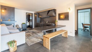 A modern kitchen with dark cabinetry, a wooden bench, and a dining area. - Lake Como View 3BR | Regina 35 (Carate Urio)