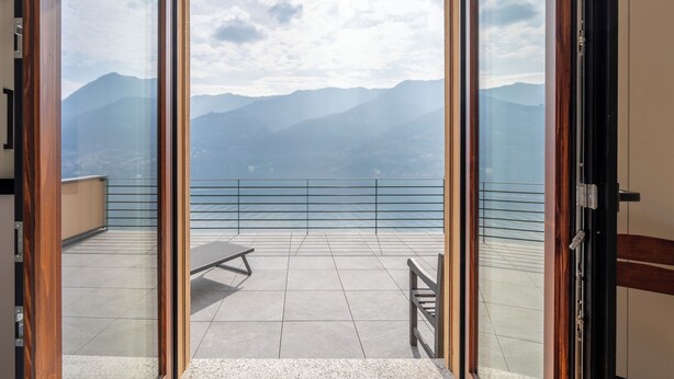 A balcony with a view of mountains, a table, and a chair. - Lake Como View 3BR | Regina 35 (Carate Urio)