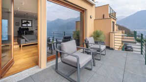 A modern outdoor patio with seating, a glass door leading to an interior living area, and a mountain view. - Lake Como View 3BR | Regina 35 (Carate Urio)