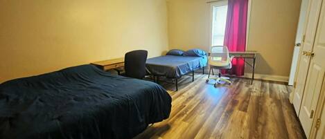 A room with two beds, a desk, a chair, and a ceiling fan.