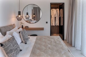 A bedroom with a bed, pillows, a round mirror, pendant lights, a robe rack, and a wooden shelf. - Olea Hill Villas - Luxury Villa Lamina, by Estia (Vathianos Kampos)