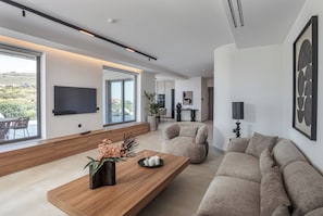 Ein modernes Wohnzimmer mit Couchtisch aus Holz, beiger Couch und an der Wand montiertem Fernseher.