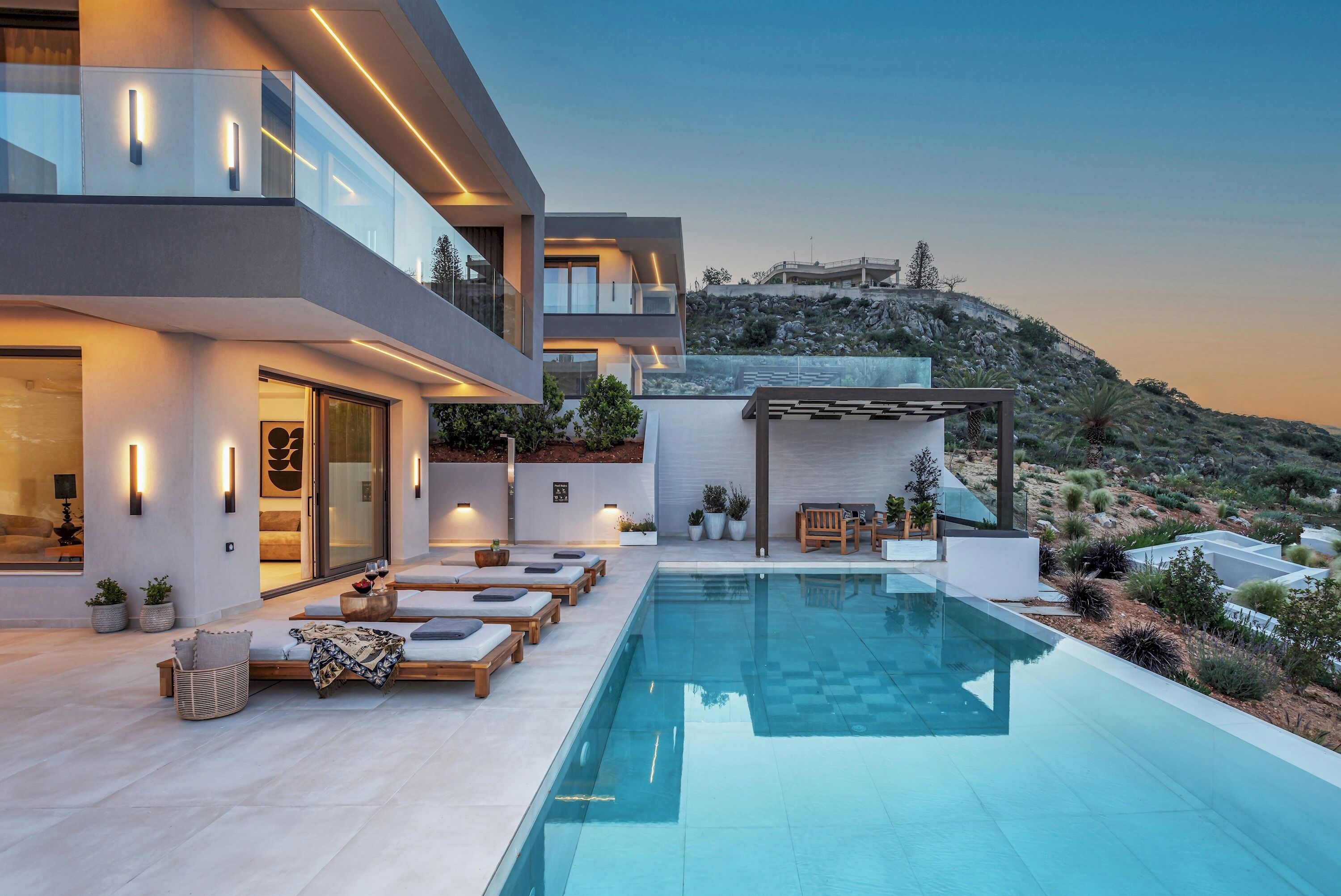 A modern house with a swimming pool, outdoor seating, and a view of a hill.
