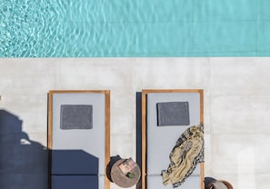 Two sun loungers with towels and a hat, a pool with clear water, and a tiled floor. - Olea Hill Villas - Luxury Villa Lamina, by Estia (Vathianos Kampos)