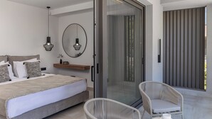 A modern bedroom with a bed, two wicker chairs, a small table with a cup and cookies, a mirror, and a sliding glass door leading to a balcony. - Olea Hill Villas - Luxury Villa Lamina, by Estia (Vathianos Kampos)