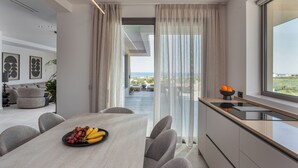 A modern kitchen with a dining area, a view of the outdoors, and a fruit bowl on the table. - Olea Hill Villas - Luxury Villa Lamina, by Estia (Vathianos Kampos)