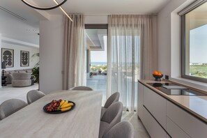 Eine moderne Küche mit Essbereich, Blick ins Freie und einer Obstschale auf dem Tisch.