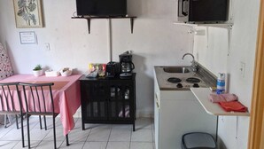 Eine kompakte Küche mit Mikrowelle, Herd und Kaffeemaschine. Es gibt eine kleine Essecke mit Tisch und Stühlen.