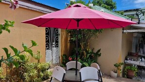 Eine Terrasse mit Tisch, Stühlen, einem Sonnenschirm und Kübelpflanzen.